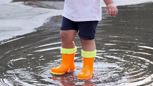 小孩穿着橙色靴子在雨后在水坑里玩13秒视频