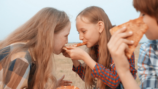顽皮的少女在干草堆背景的乡村田野上吃两个披萨。快乐的少年朋友在农村野外野餐时吃披萨视频