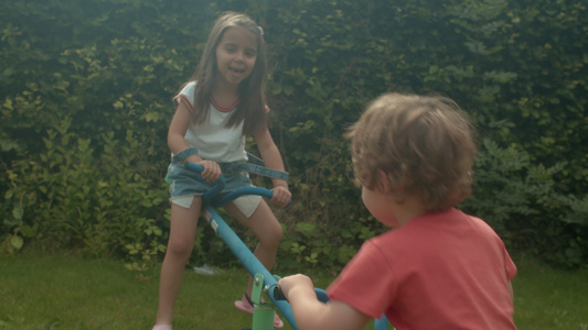 年轻的男孩和女孩在花园里玩跷跷板。视频