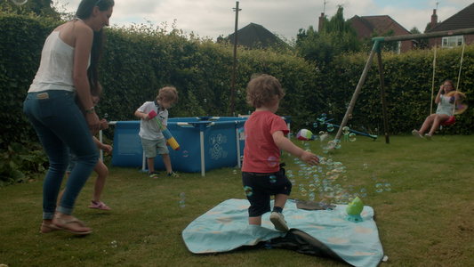 一群孩子在有秋千和戏水池的花园里玩肥皂泡泡视频