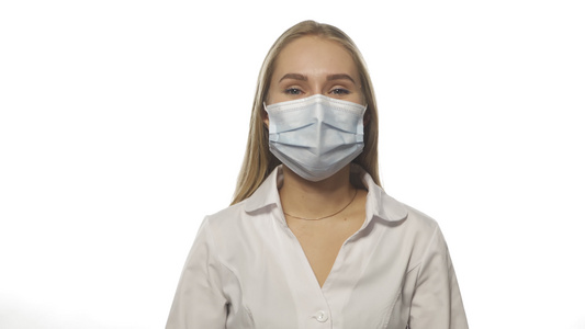 年轻的金发医生戴着紫色一次性手套固定医用口罩，看着镜头。在白色背景上隔离。高品质 4k 分辨率素材视频
