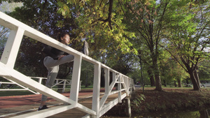 女孩在木桥围栏上伸腿,为跑跑的锻炼加热11秒视频