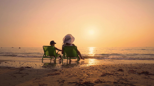 日落时坐在椅子上,在海滩玩的帽子是母亲和儿子的怀尔斯帽,友好家庭的概念视频