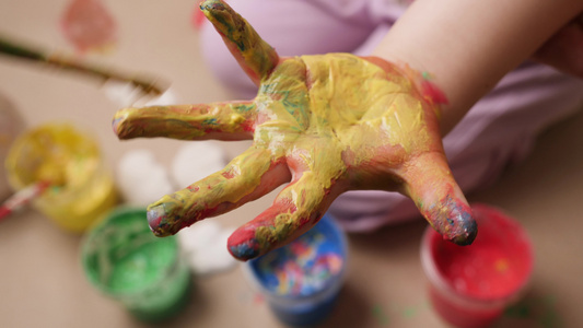 画儿童手绘彩色油漆女孩婴儿艺术家孩子创意儿童教育。蹒跚学步的手指画手孩子艺术手宝贝。孩子画她的手画笔关闭婴儿手视频