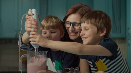 幸福的母亲和两个孩子在家里的蓝色厨房里用搅拌机烹制草莓视频