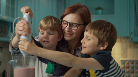 幸福的母亲和两个孩子在家里的蓝色厨房里用搅拌机做果汁视频