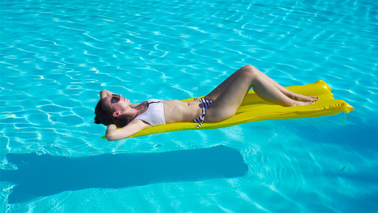 年轻妇女在户外游泳池的空气床垫上放松视频