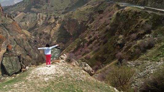 蓝褐发女孩享受着不可思议的自然景观 山谷地貌在悬崖上 悬崖俯视山谷视频
