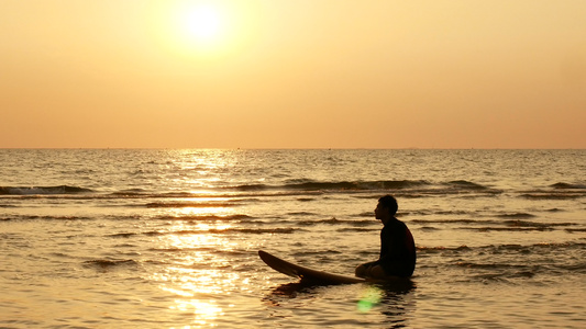 在热带海滩日落时 坐在海上冲浪板上的冲浪男子的休眠视频