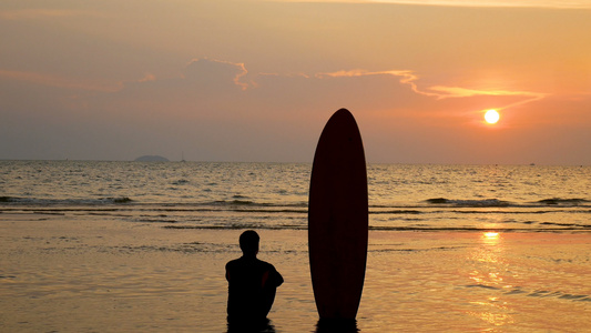 坐在海边的冲浪者男子的背影,在热带海滩日落时有长长的冲浪板视频