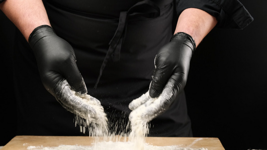 黑乳胶手套主厨在圆木板上喷洒白面粉、黑色背景、慢动作视频