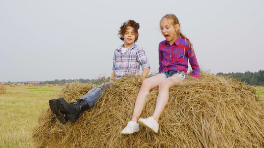 慢动作女孩和男孩在农村的收割场跳跃干草堆。快乐的青少年女孩和男孩在农田的干草堆上玩乐。孩子们在干草堆上撒干稻草视频