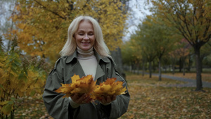 在秋天公园里慢动作的和叶子玩得开心的年长女士13秒视频