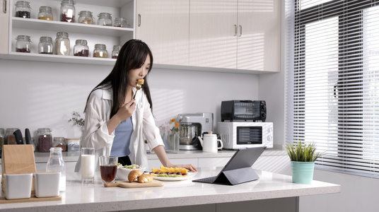 女性在厨房吃水果看电脑视频