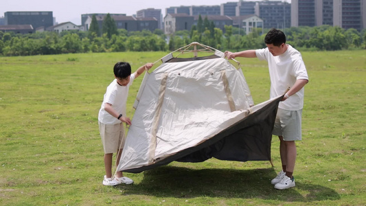 年轻家庭户外露营 父子合作搭帐篷慢镜视频