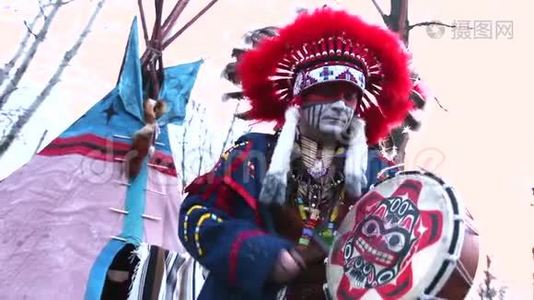 穿着全套衣服的北美印第安人，一个穿着西装的印第安人，在wigwam前面的街道上和一只手鼓跳舞视频