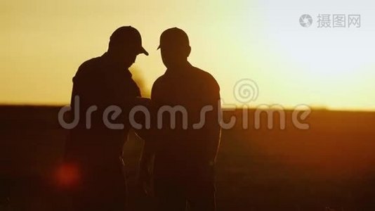 做农业综合企业的生意。 两个男农在田间交流，用平板握手. 日落时剪影视频