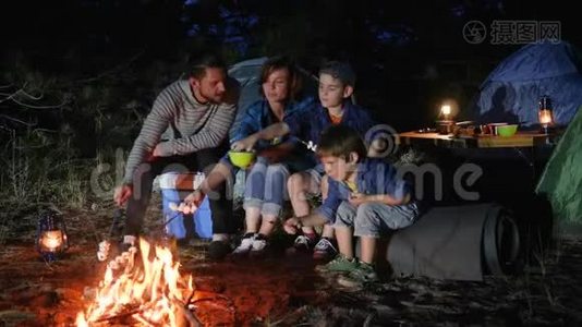 父母带着孩子在篝火上烤棉花糖到林地，幸福的家庭在大火中煎棉花糖视频