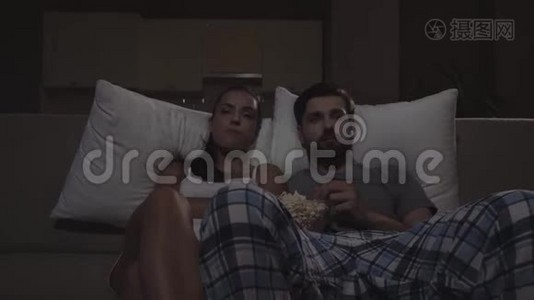 男人和女人坐在沙发上看电影。 他们吃爆米花。 女孩开始睡着了。 他们看起来视频