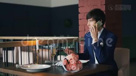 一个脾气暴躁的家伙用手机和他的女朋友聊天，他一个人坐在餐馆里等着，然后拿着花和鲜花视频