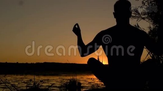 日落时在海滩上练习瑜伽的年轻人剪影。 4K视频