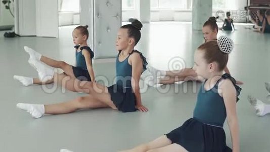 孩子们上舞蹈课。 小女孩坐在地板上，重复老师后面的动作视频