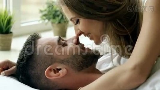 一对年轻、美丽、有爱心的夫妇早上在床上玩耍和接吻。 迷人的男人亲吻拥抱他视频