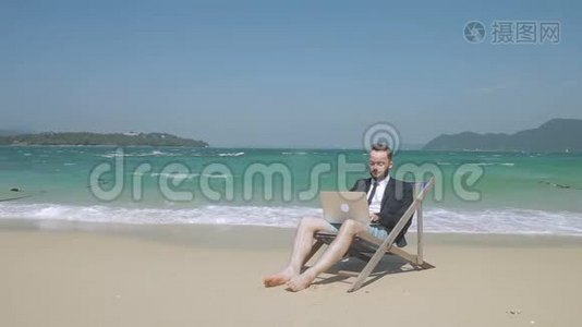 在海滩上，笔记本电脑后面的年轻人在度假时做生意。视频
