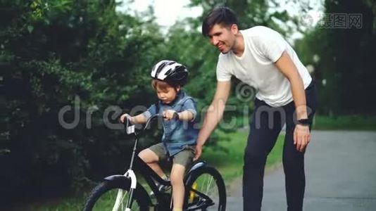 当他细心的父亲帮他拿着自行车教书时，兴奋的男孩骑着自行车笑得很慢视频