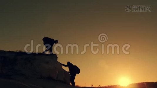 在两个登山者之间帮忙的剪影。 山顶上有两个徒步旅行者，一个人帮助一个人爬上一个纯粹的地方视频