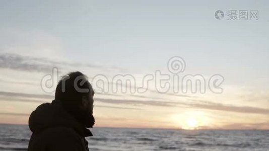 年轻人独自走在海边，望着海浪。 男人在海滩上享受日落。视频
