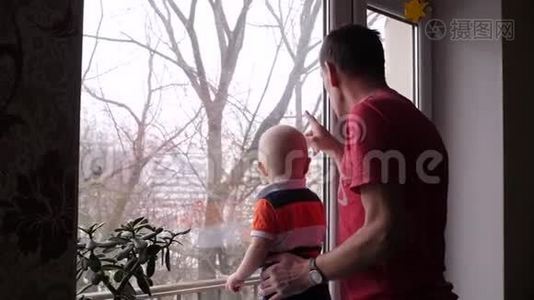 一位老人和他可爱的小孙子在窗边玩耍，爷爷给小男孩看了一只鸟。视频