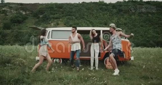 充满魅力的年轻一群朋友在大自然中跳舞，在田野的中央，在一辆复古的面包车后面。 4k视频