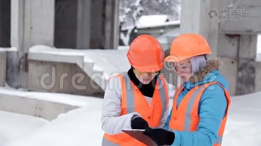 建筑工人和工程师在施工现场交谈。 在大楼外戴头盔的工人视频