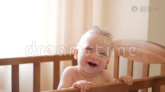 婴儿`站在家里的婴儿床上。 小男孩学着站在婴儿床上。视频