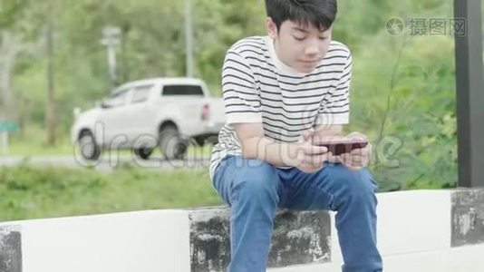亚洲十几岁的男孩在路边玩手机游戏视频