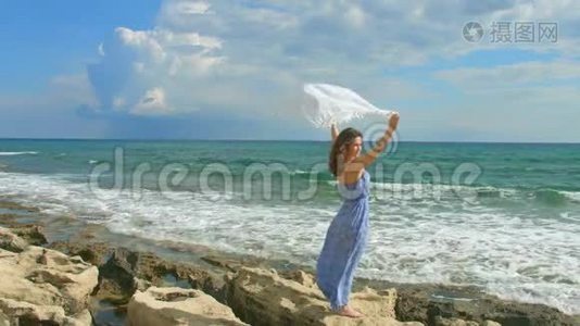 美丽的女士穿着长裙，在岩石海滩上挥舞着白色的围巾视频