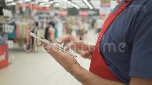穿红色围裙的销售人员使用的数字平板电脑，背景是商店视频