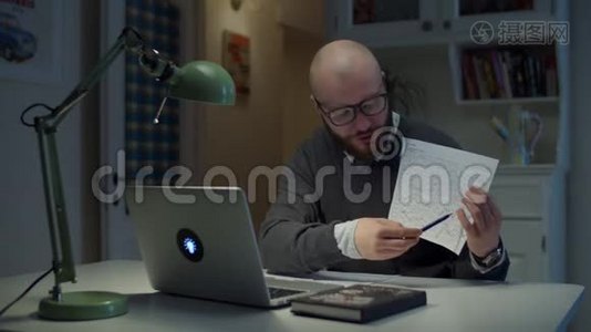 30多岁的留着胡子的戴眼镜的男人，给在家里看笔记本电脑的学生展示一张有图表的纸。在线教育视频
