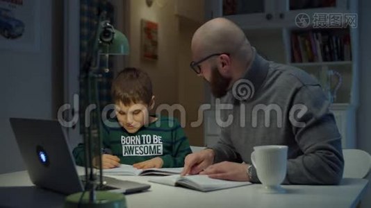 年轻的30岁的父亲和上学的儿子在家做网上作业。 戴眼镜的胡子男在网上学习视频