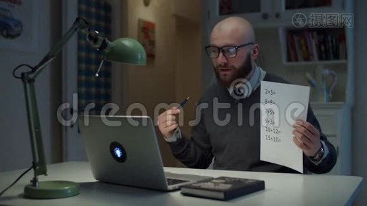 30多岁的留着胡子的戴眼镜的男人在家里用简单的数学公式看着笔记本电脑。在线的视频