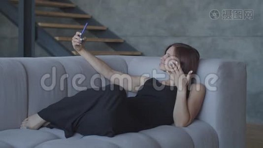 漂亮的30多岁的女人喜欢坐在舒适的沙发上用智能手机聊天。 穿着黑色衣服的漂亮女人视频