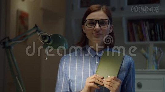 30多岁的女人戴着眼镜，在家里拿着纸书和相机解释。 在线教育过程。 网络摄像机视图视频