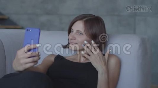 漂亮的30多岁的女人喜欢坐在舒适的沙发上用智能手机聊天。 穿着黑色衣服的漂亮女人视频