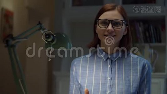 30多岁的戴眼镜的女人情绪化地说着话，大拇指朝上看着家里的相机。在线教育过程。网络摄像头视图视频