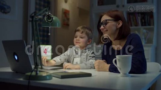 30多岁的妈妈在家和学龄前的儿子一起做网络作业。小男孩在笔记本电脑屏幕上显示正确答案视频