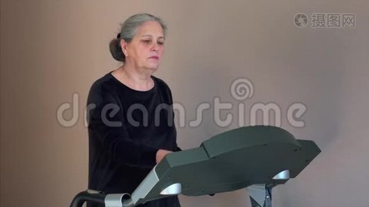年长的白发妇女在家训练前改变了跑步机的模式。视频