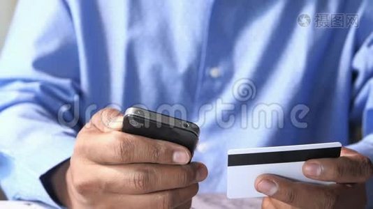 男人`手拿着信用卡，用智能手机上网购物视频