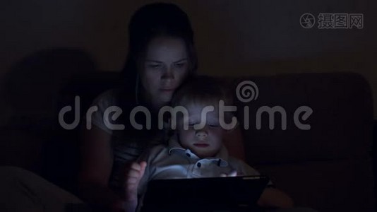 一幅母亲和儿子在黑暗中带着平板电脑在家里的肖像。视频