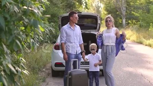 一个幸福的家庭的肖像，一个手提箱靠近一条空路上的汽车后备箱视频